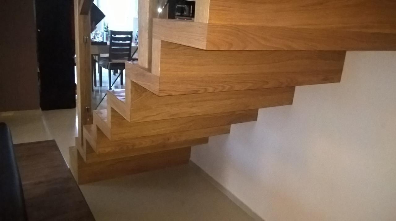 Detal drewnianych schodów wspornikowych z widocznym usłojeniem drewna dębowego, zamontowanych przy białej ścianie w nowoczesnym wnętrzu.