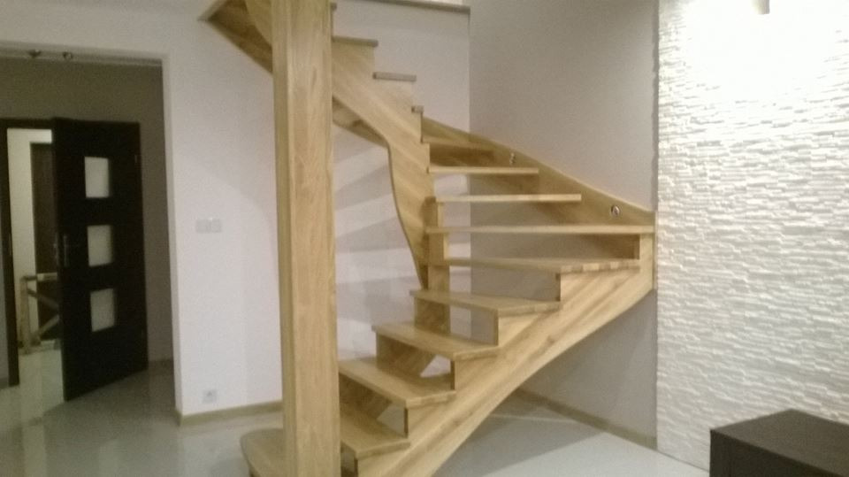 Spiralne schody z jasnego drewna z centralnym słupem, zamontowane w nowoczesnym wnętrzu z dekoracyjną ścianą o fakturze kamienia.