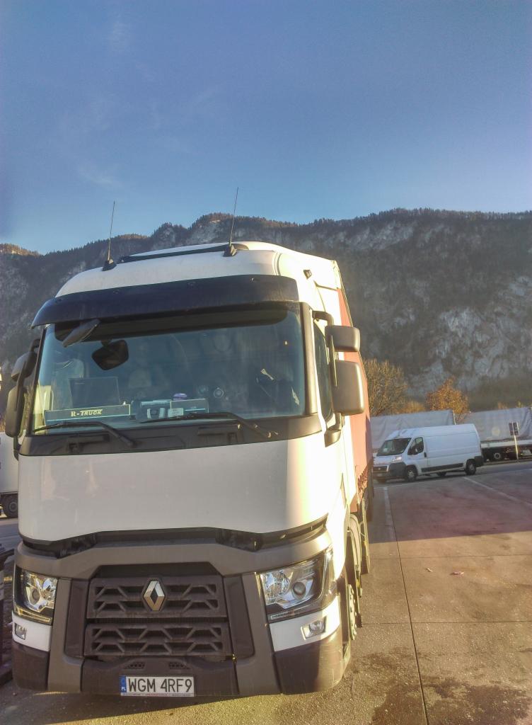Biała ciężarówka Renault z widoczną tablicą rejestracyjną WGM 4RF9, zaparkowana na betonowym placu z widokiem na zalesione góry w tle, obok zaparkowany biały bus.
