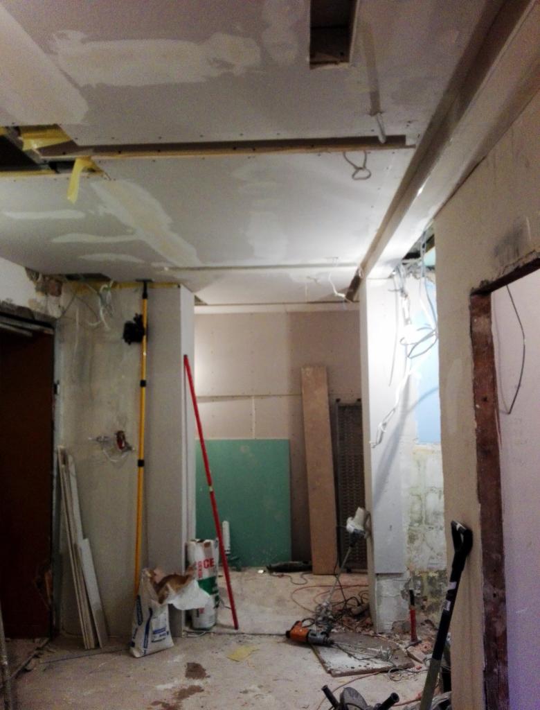 Wnętrze w trakcie prac: sufit z płyt kartonowo-gipsowych, widoczne kable, narzędzia i materiały budowlane, poziomica oparta o ścianę.