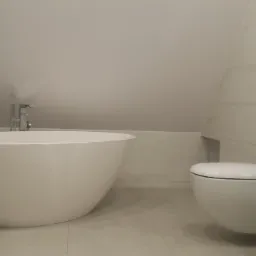 Nowoczesna łazienka na poddaszu z wolnostojącą wanną, podwieszaną toaletą i białą umywalką nablatową na szafce z szufladami.