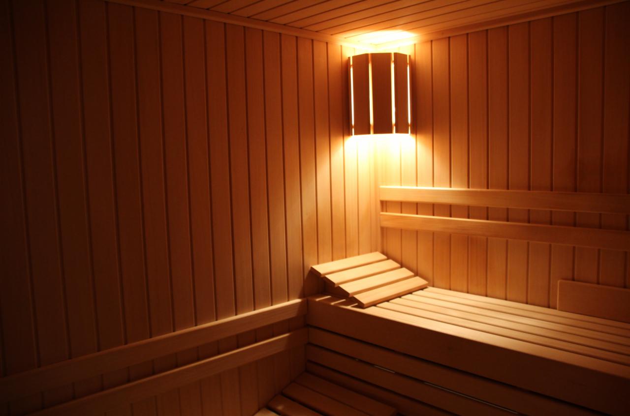 Wnętrze drewnianej kabiny z ławkami i oświetleniem ściennym, ciepłe światło podkreśla naturalny kolor drewna.