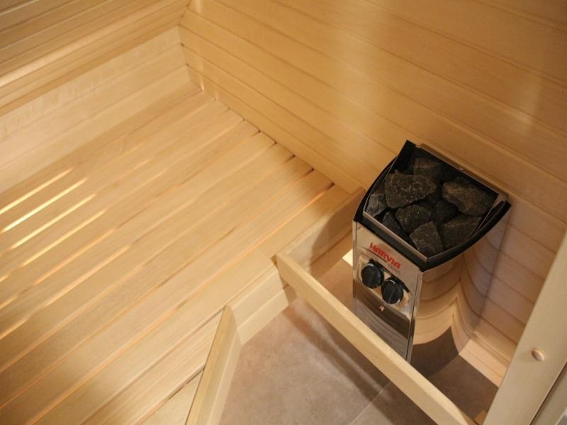 Wnętrze drewnianej kabiny z piecem Harvia wypełnionym kamieniami, widoczne jasne deski boazeryjne i fragment podłogi wyłożonej płytkami.