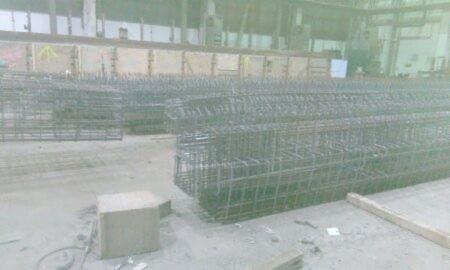 Siatki zbrojeniowe ułożone w stosy w hali produkcyjnej, widoczne drewniane skrzynie w tle.