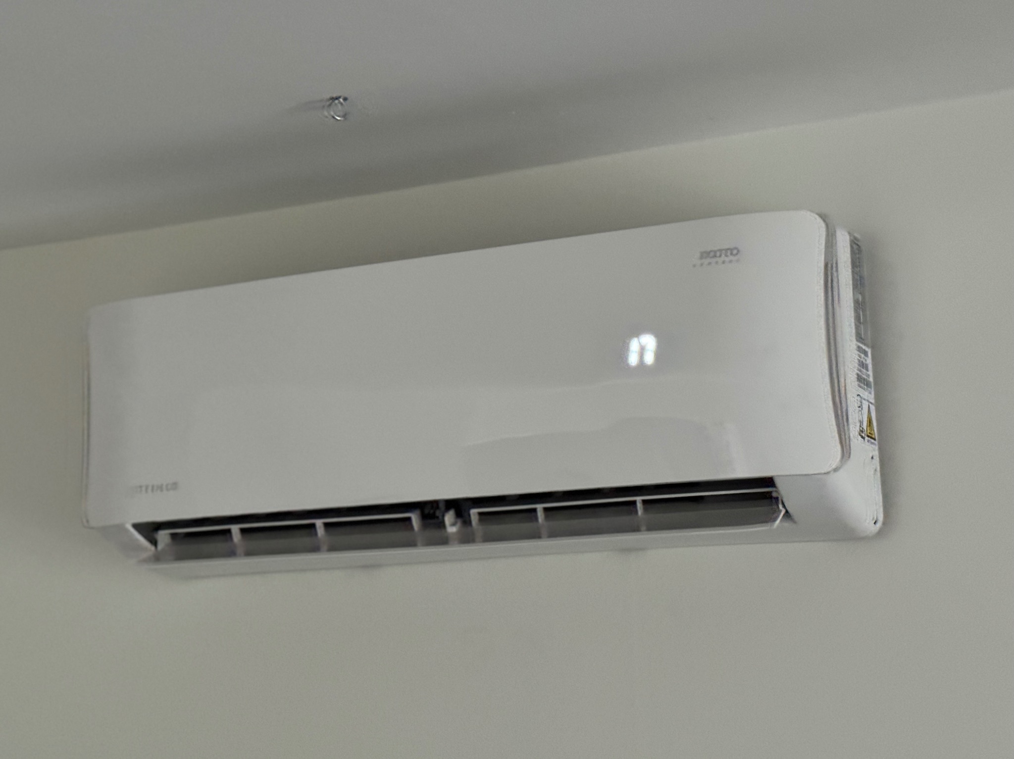 Biała, wisząca jednostka wewnętrzna klimatyzacji z wyświetlaczem temperatury na jasnej ścianie.