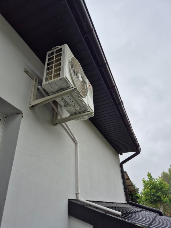 Zewnętrzna jednostka klimatyzacji zamontowana na ścianie budynku, widok z dołu, rury odprowadzające skropliny.