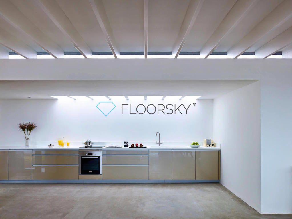 Nowoczesna kuchnia z beżowymi szafkami na tle białej ściany z logo firmy Floorsky, widoczne oświetlenie sufitowe i betonowa posadzka.