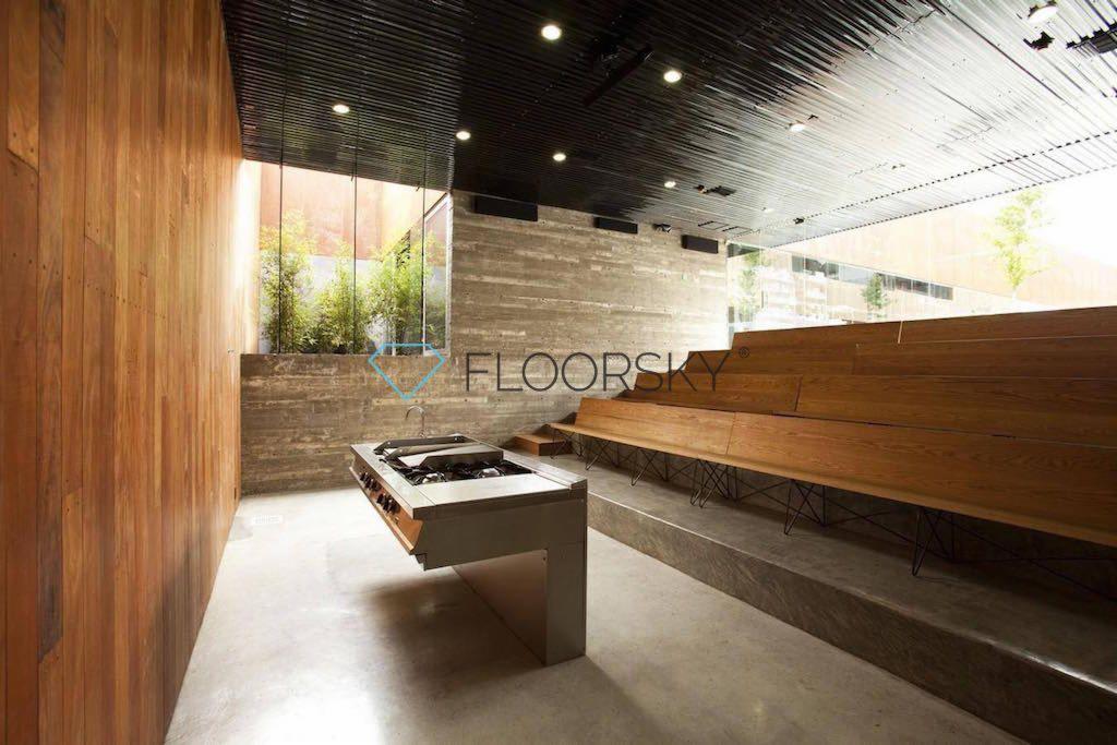 Nowoczesne wnętrze z betonową ścianą, drewnianą boazerią, podłogą z wylewki i nietypową instalacją kuchenną.