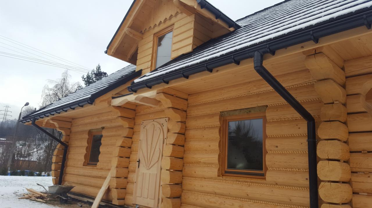 Surowy drewniany dom z bali z czarnymi rynnami i śniegiem na dachu, widok z zewnątrz, boczny kadr.