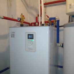 AVM ENGINEERING Sp. z o.o. - Biała jednostka centralna NIBE BA-SVM 10-200 z ekranem wyświetlającym parametry pracy, otoczona instalacją hydrauliczną z czerwonymi i niebieskimi rurami w pomieszczeniu technicznym.