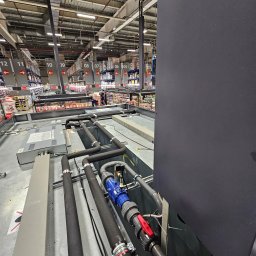 GREEN SERWIS klimatyzacja-chłodnictwo-wentylacja Rafał Zieliński - Instalacja rur chłodniczych z zaworami w supermarkecie, widok z góry na system chłodzenia, rury w izolacji, elementy instalacji na tle regałów sklepowych.