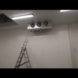 Wnętrze chłodni z zamontowanym agregatem chłodniczym sufitowym z trzema wentylatorami i rozstawioną drabiną aluminiową.