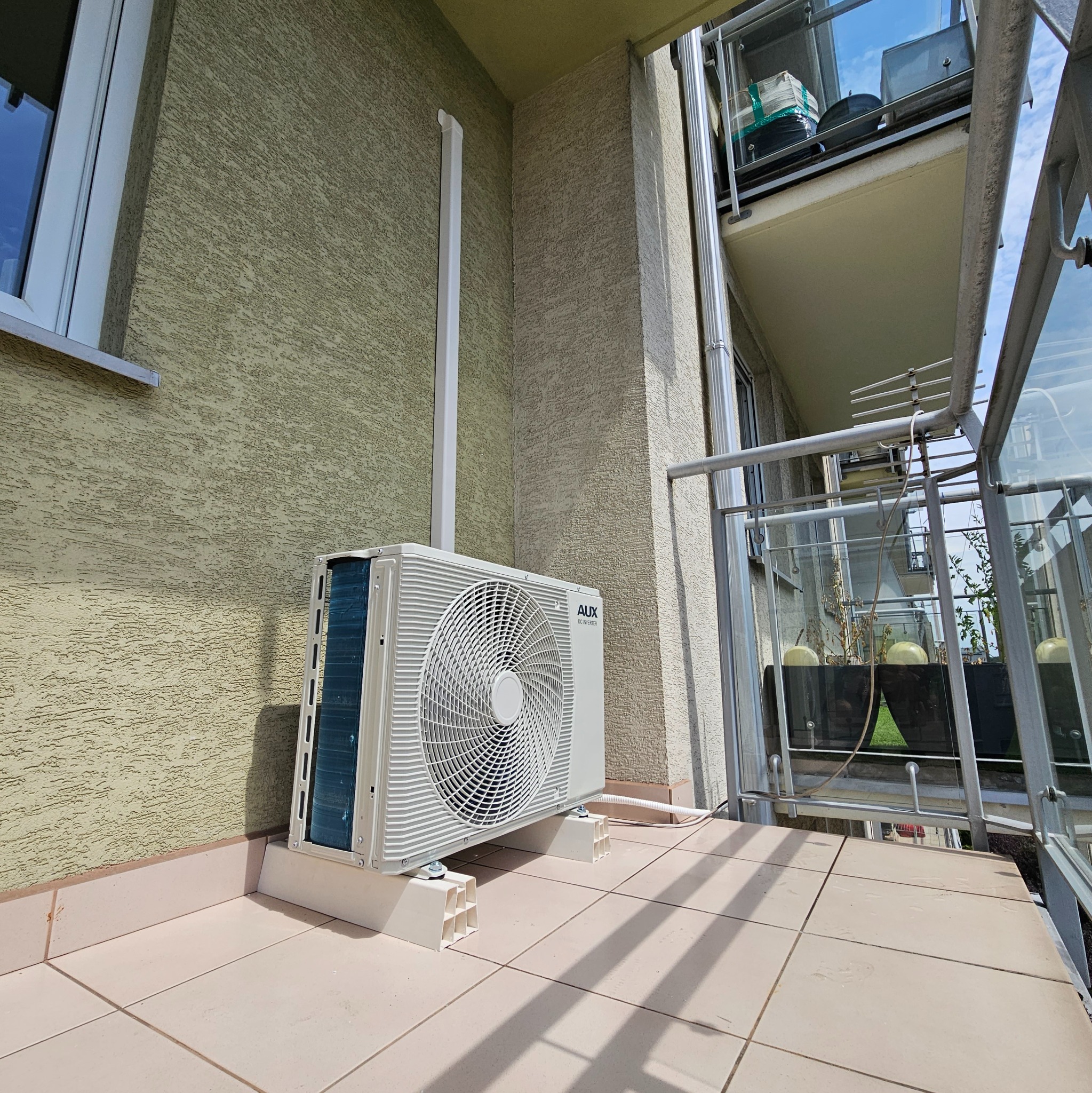 Zewnętrzna jednostka klimatyzacji AUX DC Inverter zamontowana na balkonie, widoczna instalacja odprowadzająca skropliny po elewacji.