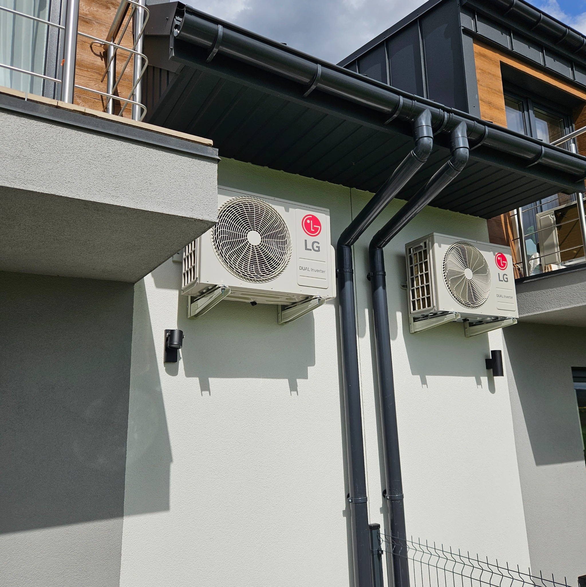 Dwa klimatyzatory LG Dual Inverter zamontowane na elewacji nowoczesnego domu, widoczne rury odprowadzające skropliny.