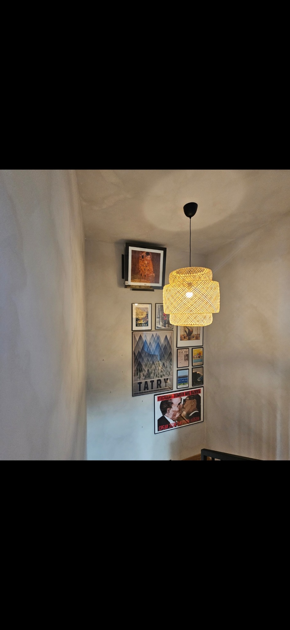 Wnętrze z dekoracyjną lampą rattanową i galerią plakatów na ścianie, w tym plakat z motywem Tatr.