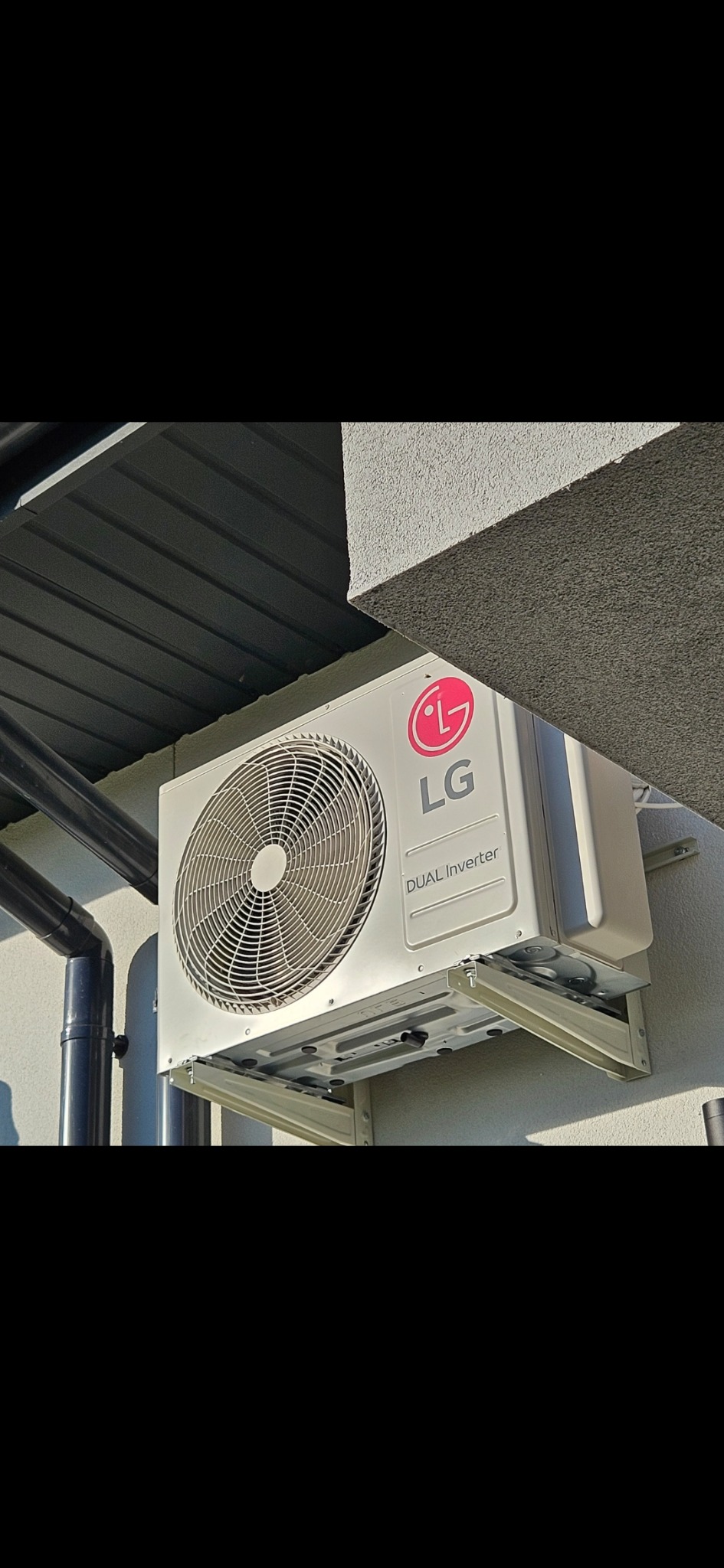Zewnętrzna jednostka klimatyzatora LG Dual Inverter zamontowana na ścianie budynku z widocznymi wspornikami montażowymi i rurami odprowadzającymi skropliny.