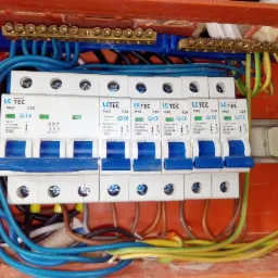 Rozdzielnica elektryczna z zainstalowanymi bezpiecznikami automatycznymi LC TEC, widoczne przewody w kolorach niebieskim, żółto-zielonym i brązowym. Widoczne oznaczenia na bezpiecznikach: M60, B10,...