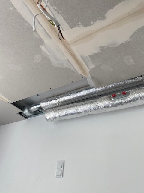 Sufit z płyt kartonowo-gipsowych w trakcie montażu, widoczne przewody elektryczne, instalacja wentylacyjna w izolacji aluminiowej, ściana z włącznikiem światła.