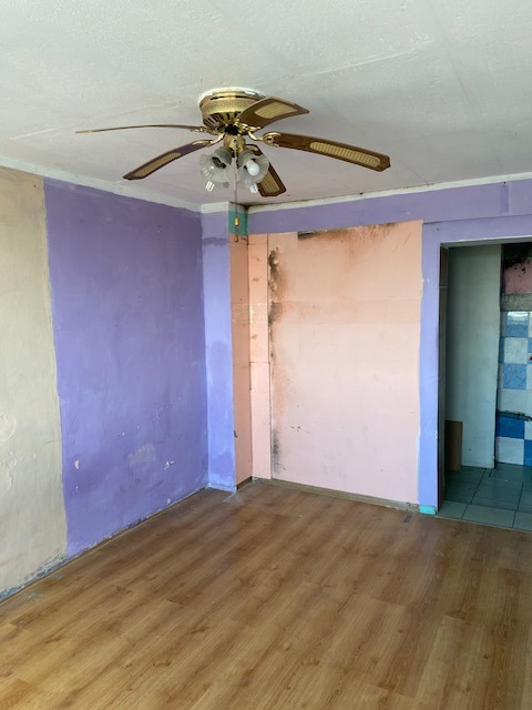 Pokój w trakcie przygotowania do malowania: ściany częściowo pomalowane na fioletowo, częściowo przygotowane do malowania, drewniana podłoga, sufit z wentylatorem i lampami.