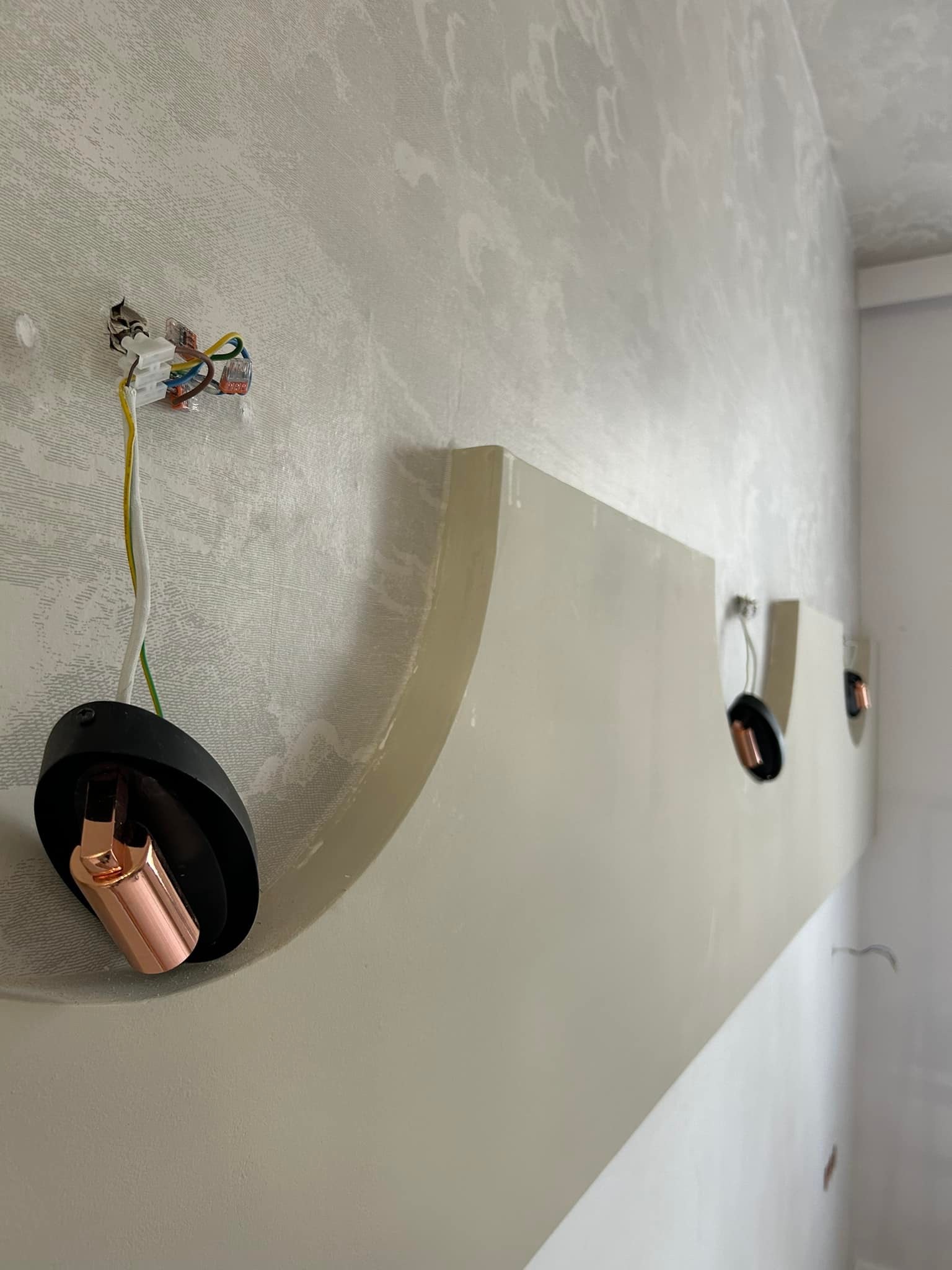 Montaż dekoracyjnego oświetlenia ściennego z miedzianymi akcentami na tle wzorzystej ściany, widoczne kable i złączki elektryczne.