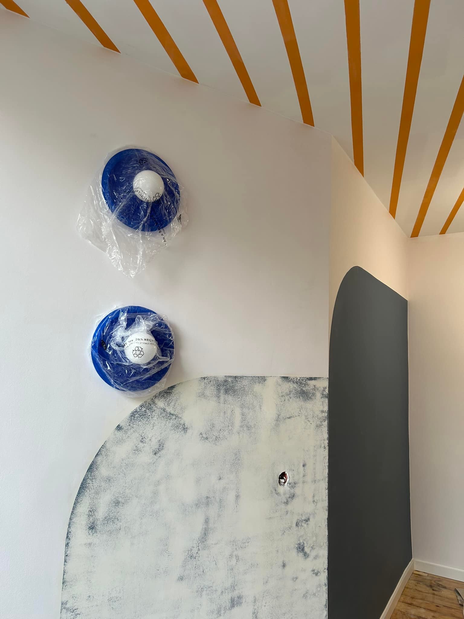 Wnętrze w trakcie malowania: widoczne pomalowane na szaro łuki na ścianie, przygotowana do malowania ściana z widocznym gniazdkiem elektrycznym, dwa zabezpieczone folią detektory dymu na suficie...