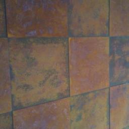 DecorLine - Ściana pokryta kwadratowymi panelami z efektem rdzy, widoczne nieregularne wzory i odcienie brązu, pomarańczy i szarości.