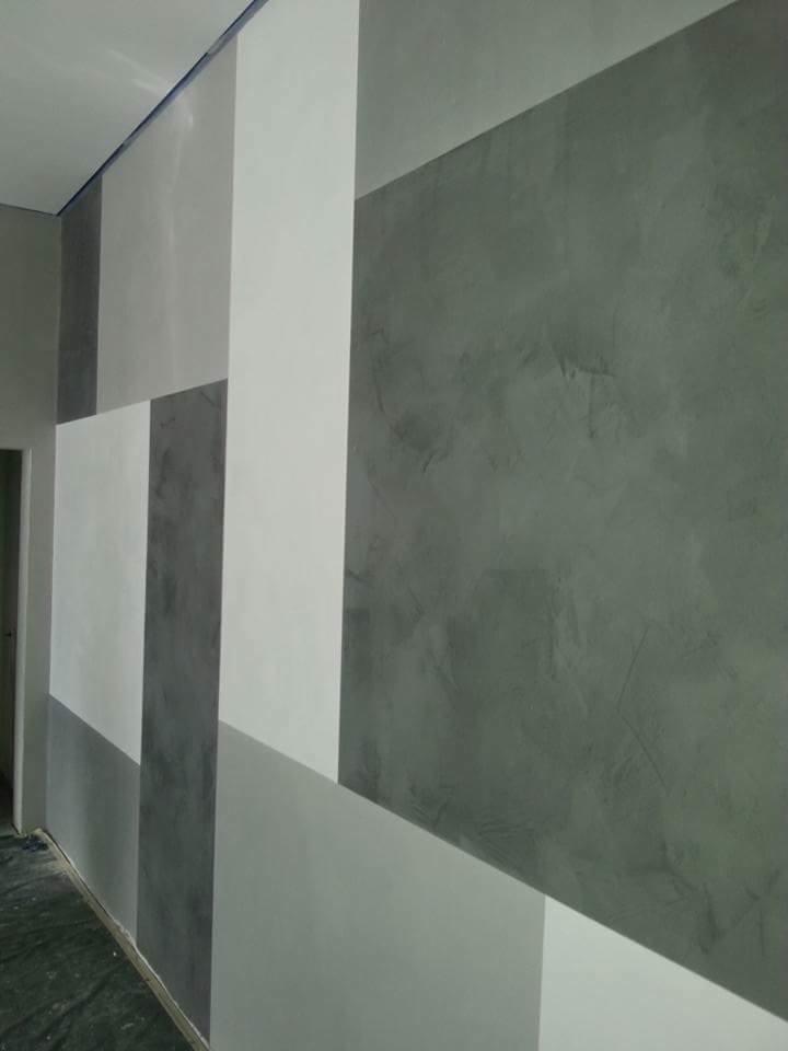 Geometryczny wzór na ścianie w odcieniach szarości i bieli, z efektem dekoracyjnej faktury, widoczne zabezpieczenie podłogi folią.