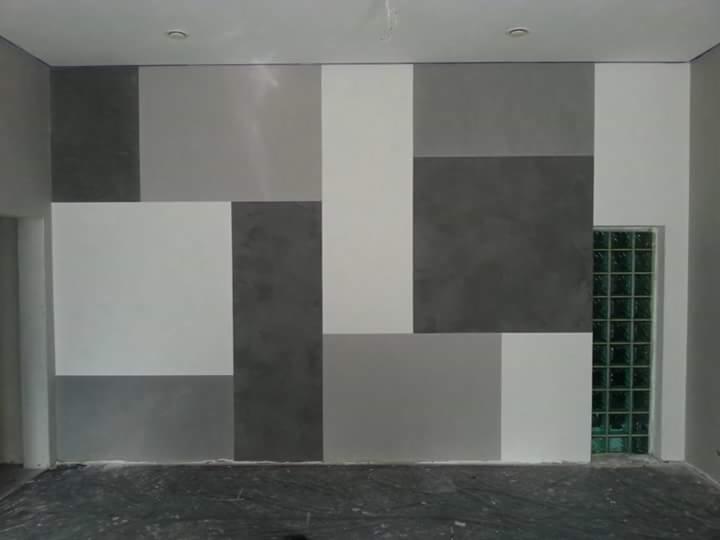 Ściana z geometrycznym wzorem w odcieniach szarości i bieli, obok luksfery, podłoga zabezpieczona folią malarską.