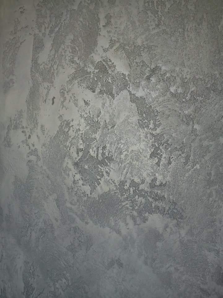 Ściana z dekoracyjną fakturą w odcieniach szarości i bieli, imitująca efekt kamienia lub betonu z widocznymi śladami pędzla.