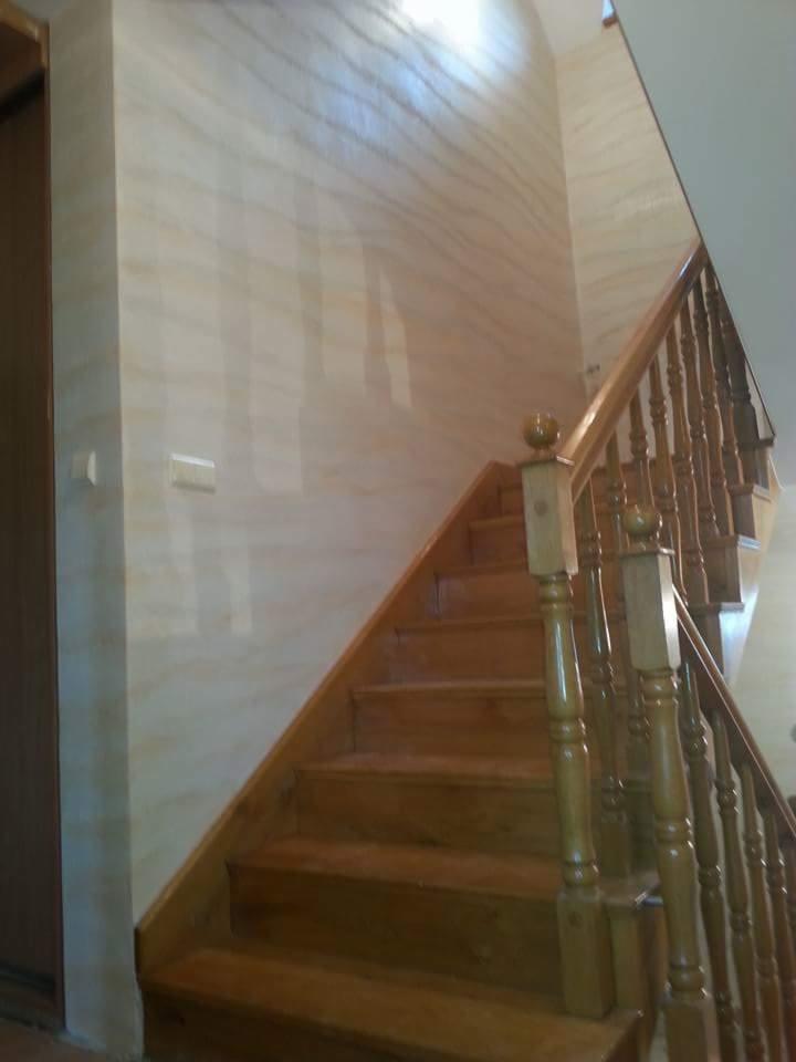 Ściana w korytarzu wykończona dekoracyjną techniką imitującą naturalny kamień, widoczne drewniane schody z balustradą.