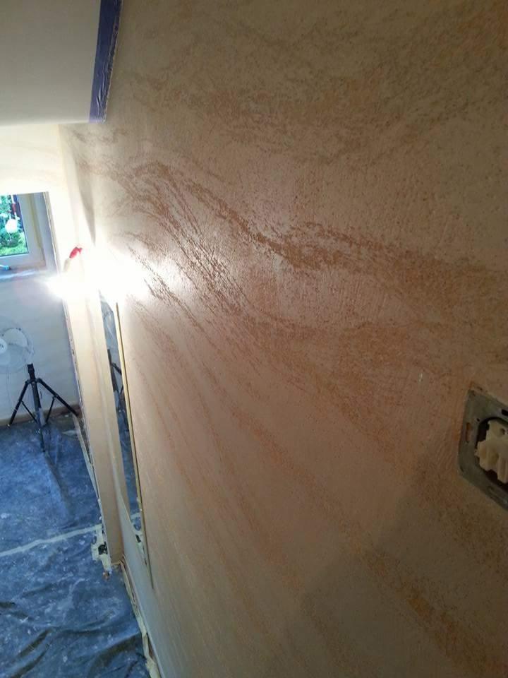 Ściana z efektem dekoracyjnym w odcieniach beżu i brązu, widoczne zabezpieczenia folią malarską, lampa na statywie i niedokończone gniazdko elektryczne.