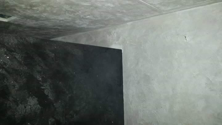 Fragment ściany i sufitu po nałożeniu dekoracyjnej, szarej struktury przypominającej beton i czarnej ściany z efektem połysku, widoczne niedoskonałości i nierówności.