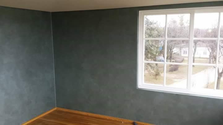 Pokój z ciemnoszarymi ścianami wykończonymi z efektem dekoracyjnym, drewnianą podłogą i białym oknem z widokiem na zewnątrz.