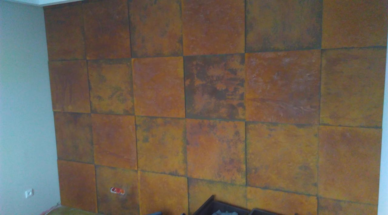 Ściana w Sobolewie wykończona kwadratowymi panelami dekoracyjnymi w odcieniach brązu i rdzy, tworzącymi efekt rustykalny.