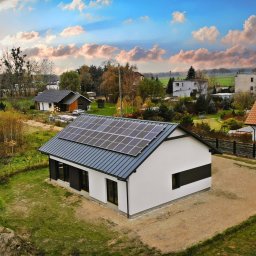 LignumHome - Budownictwo Szkieletowe - Nowoczesny dom szkieletowy z panelami słonecznymi na dachu, widok z góry na tle wiejskiego krajobrazu i zachmurzonego nieba.