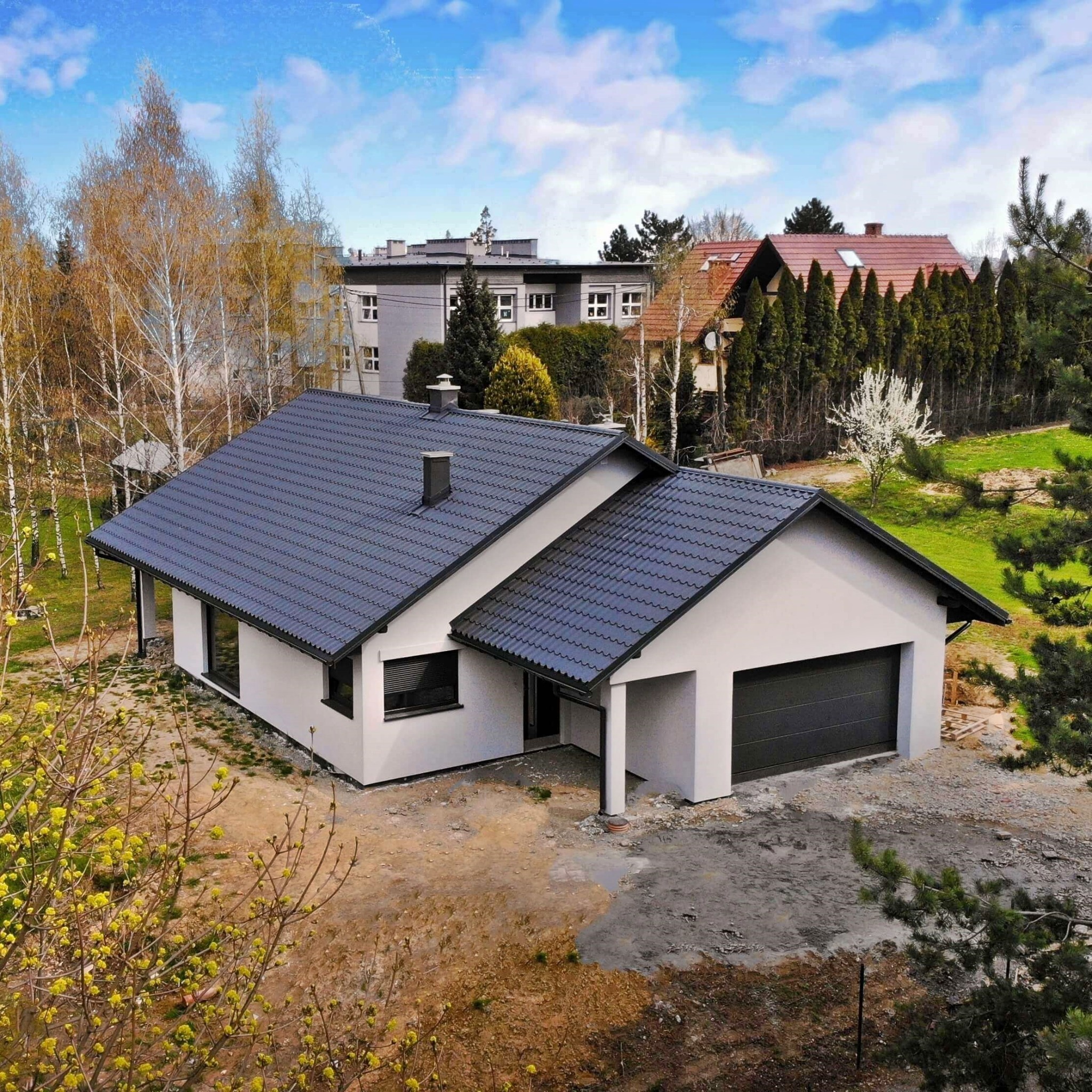 Nowoczesny, parterowy dom z garażem w trakcie wykończenia terenu, widok z góry, szara dachówka i elewacja.