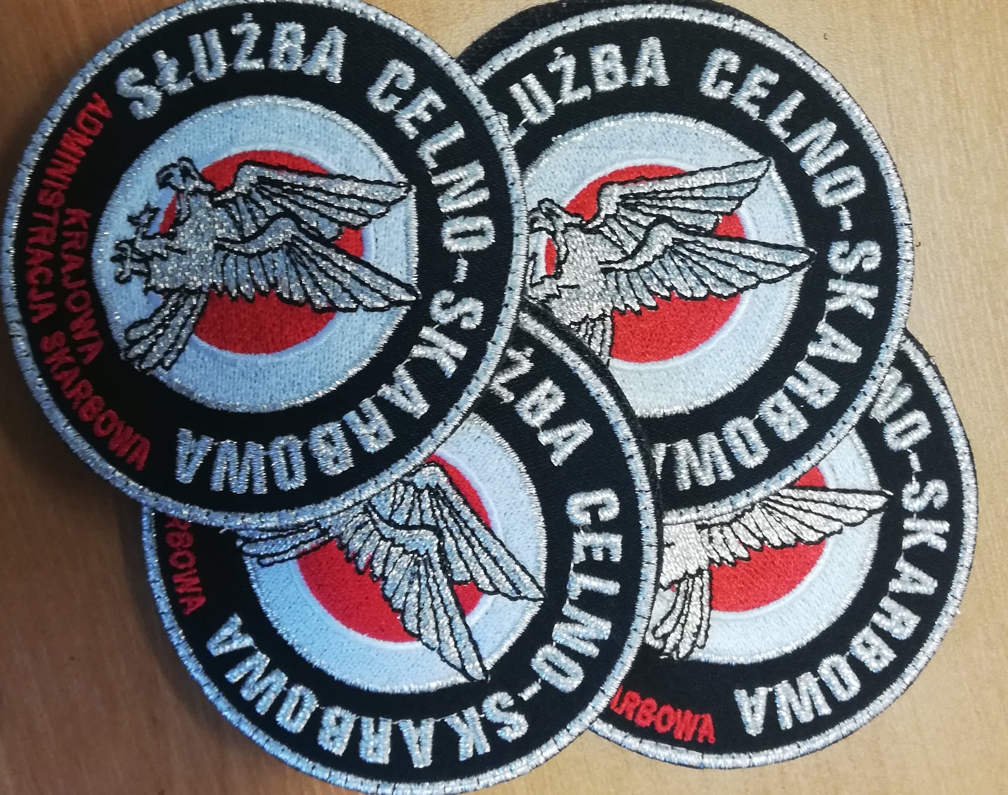 Cztery okrągłe naszywki z wyhaftowanym orłem w kolorach srebrnym, czerwonym, białym i czarnym, z napisem 'Służba Celno-Skarbowa Administracja Krajowa Skarbowa'.