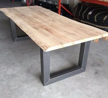 Surowy blat drewniany z naturalną krawędzią na metalowych nogach w kształcie litery U, widoczne niedoskonałości drewna, garażowe tło.