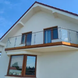Nowoczesny balkon z szklaną balustradą i drewnianym wykończeniem, widok z dołu na tle błękitnego nieba.