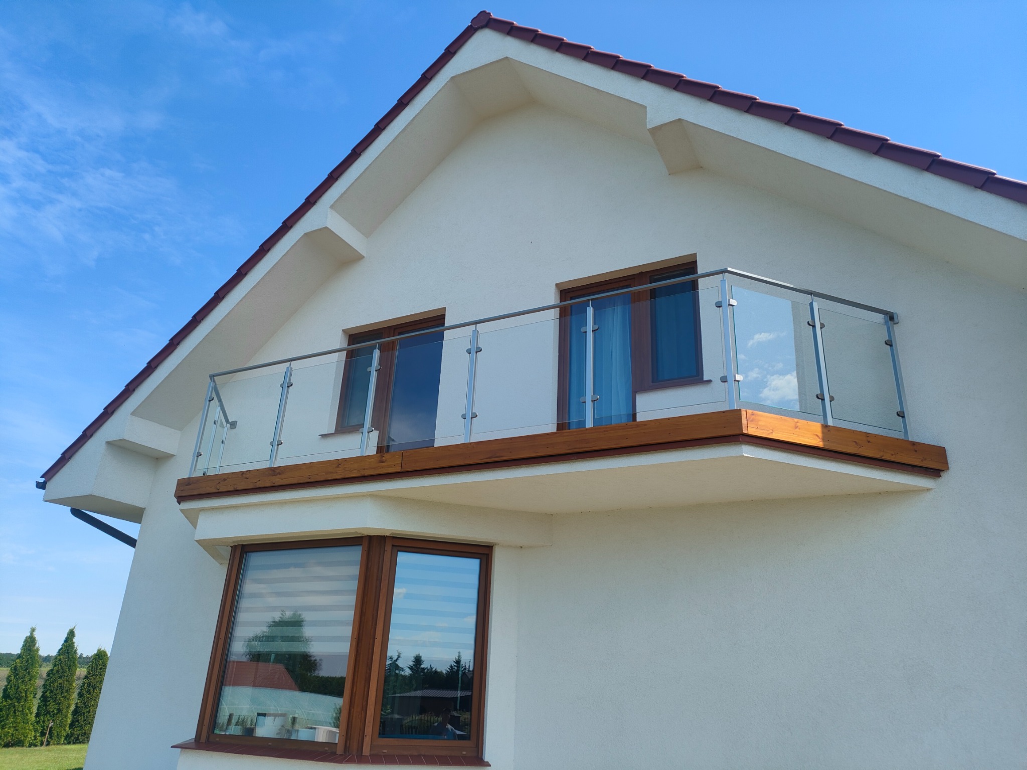 Nowoczesny balkon z szklaną balustradą i drewnianym wykończeniem, widok z dołu na tle błękitnego nieba.