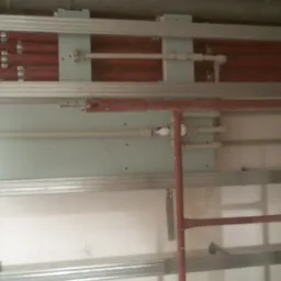 Stelaż z profili metalowych, rury instalacyjne i fragment płyty gipsowo-kartonowej w trakcie montażu, widoczna drabina malarska.