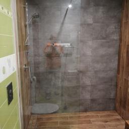 KTM-BUD JACEK LUBACZEWSKI - Nowoczesna kabina prysznicowa typu walk-in z szarą glazurą imitującą beton, drewnopodobną podłogą i zielonymi płytkami na ścianie z widoczną toaletą.