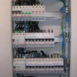 Rozdzielnica elektryczna z zamontowanymi bezpiecznikami i okablowaniem, widoczne wyłączniki główne i ochronne, opisane 'klimatyzator 1-7', przewody ułożone wewnątrz obudowy, szyna DIN z zaciskami.