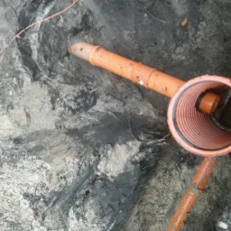 Pomarańczowa rura kanalizacyjna z uszczelką w wykopie ziemnym z widocznymi warstwami gleby.