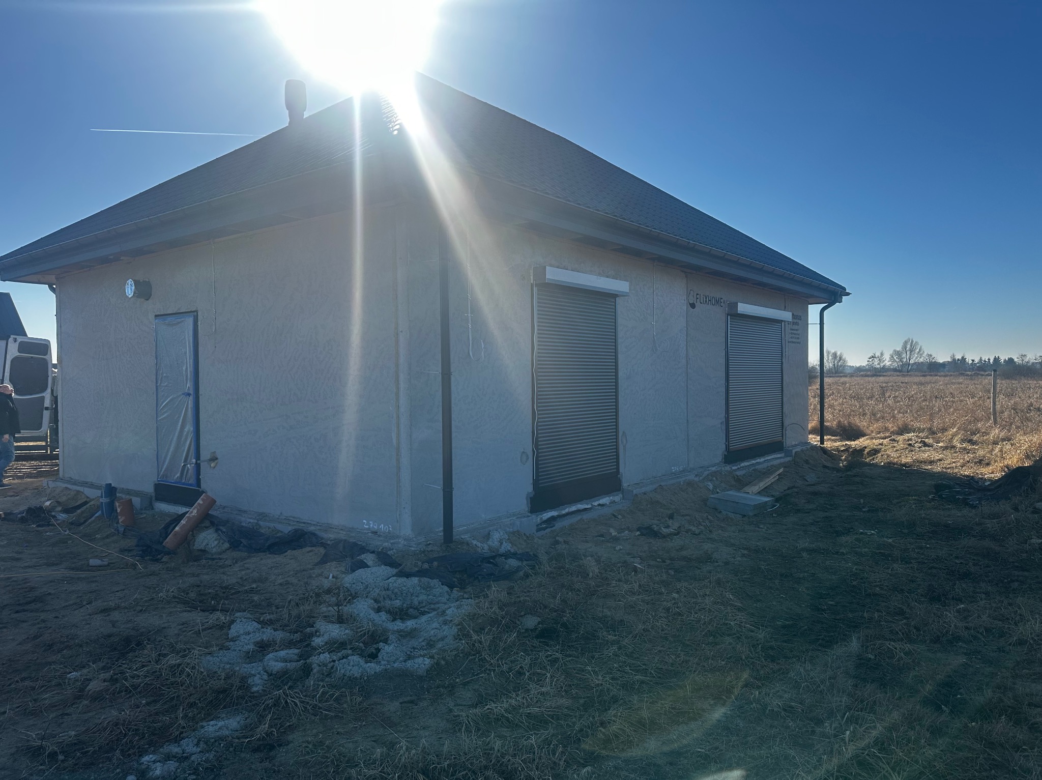 Nowoczesny budynek z zamontowanymi roletami zewnętrznymi w kolorze szarym, widoczne okno zabezpieczone folią. Słoneczny dzień.