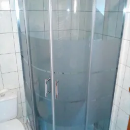 Nowa kabina prysznicowa z brodzikiem o zaokrąglonym kształcie, zamontowana w łazience z jasnymi, kwadratowymi płytkami. Kabina częściowo matowa dla prywatności.