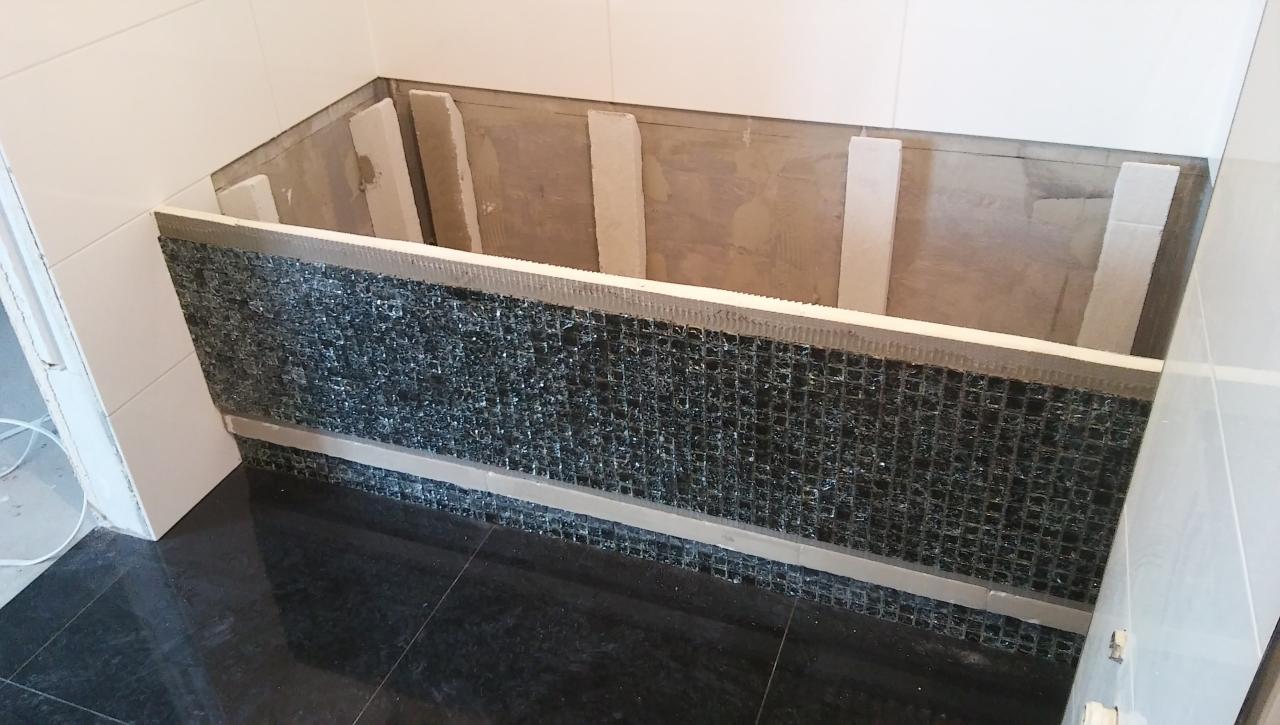 Przygotowanie obudowy wanny z mozaiki w łazience z czarną podłogą i białymi płytkami ściennymi, widoczne elementy konstrukcyjne i etap prac glazurniczych.