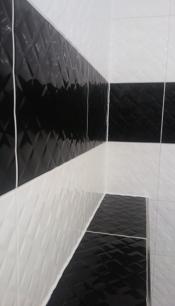 Czarno-biała ściana i półka w łazience wyłożone płytkami z wypukłym wzorem rombów, widoczne fugi.