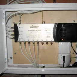 Multiswitch Signal MP-0508 zamontowany w skrzynce z otwartymi drzwiczkami, widoczne podłączenia kabli koncentrycznych i zasilanie, czerwona dioda na zasilaczu świeci.
