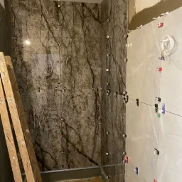 Układanie płytek w łazience; widoczne płytki imitujące marmur na jednej ścianie i jasne płytki na drugiej, system poziomowania płytek z kolorowymi klipsami, drabina oparta o ścianę.